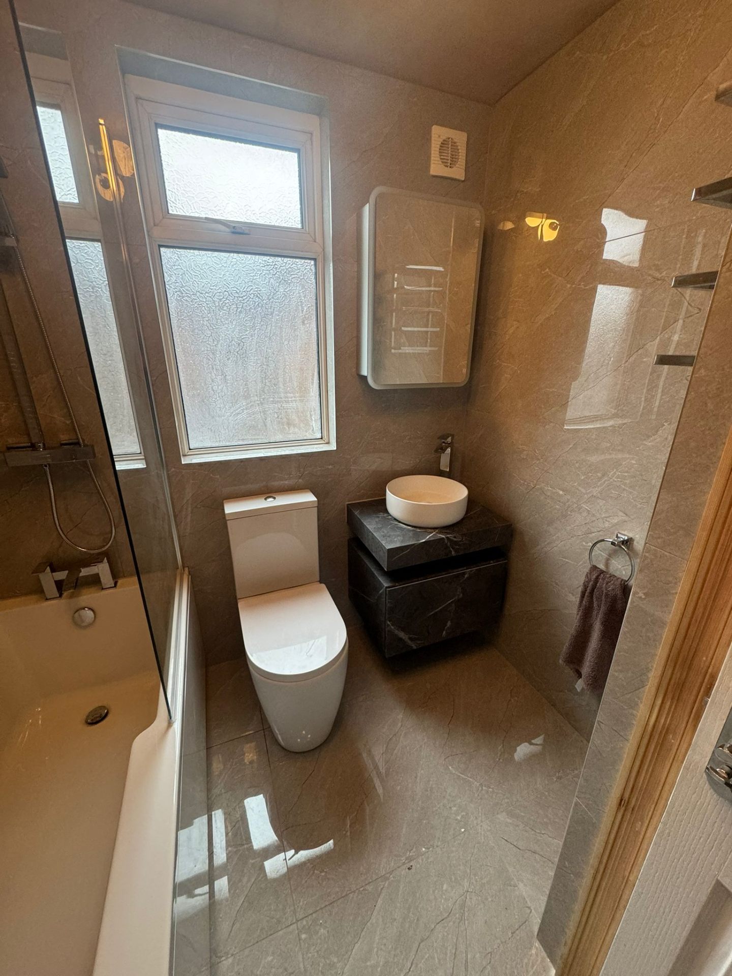 Full bathroom with wall-hung toilet, bath, and black marble vanity installed in Manchester